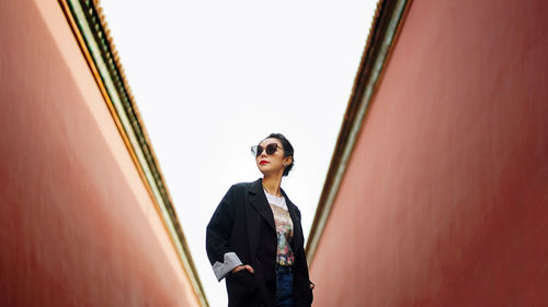 Young woman looking away while standing against wall