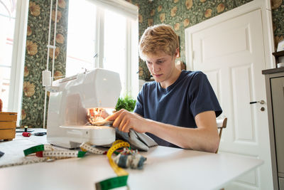 Young man sewing textile at home