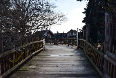 Footbridge amidst trees and buildings against sky