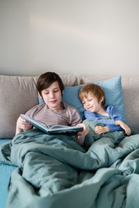 Two brothers and their domestic dog are laying in bed and reading a book together