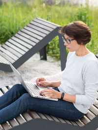 Woman sits with laptop on urban park bench. freelancer at work. student learns remotely 