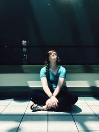 Young woman looking up while sitting on tiled floor