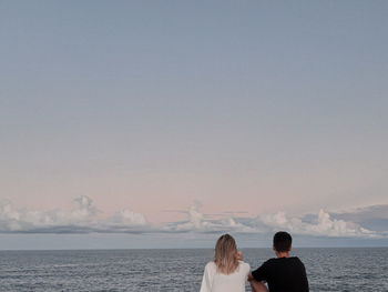 Rear view of couple looking at sea against sky during sunset