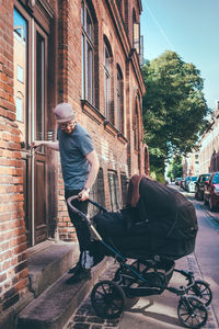 Full length of man holding baby carriage while standing at entrance on building