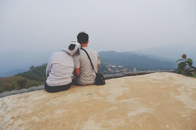 Rear view of man sitting on mountain against sky