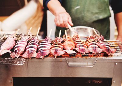 Midsection of man barbecuing squids on grill
