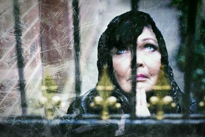 Woman praying while looking up seen through metal fence