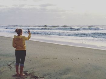 Rear view full length of woman photographing while standing at beach