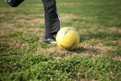 Low section of boy kicking ball while playing soccer on field