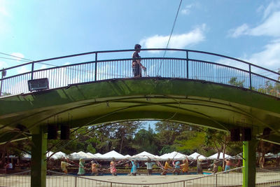 Low angle view of people standing on bridge against sky