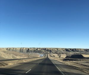 Road amidst desert against clear blue sky