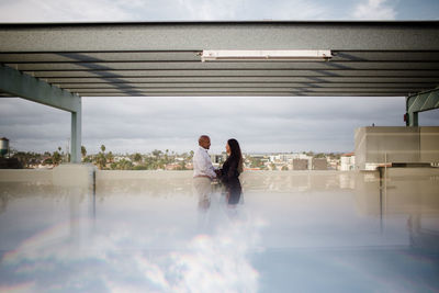 Rear view of couple walking on bridge against sky