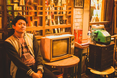 Portrait of young man sitting by television set at home