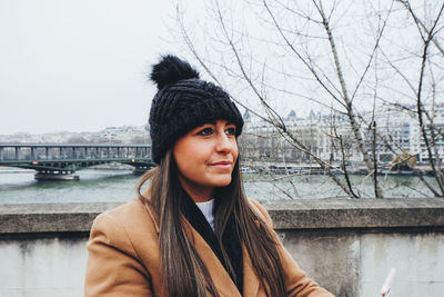 Portrait of young woman against river in winter