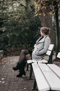 Side view of young woman sitting on bench at park