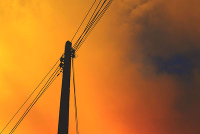 Low angle view of electric pole against orange sky