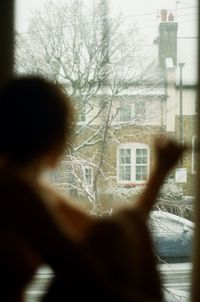 Rear view of person against building seen through window