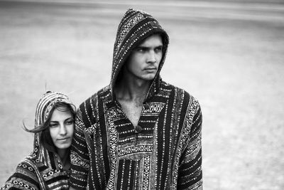 Couple in hooded clothing looking away while standing on field