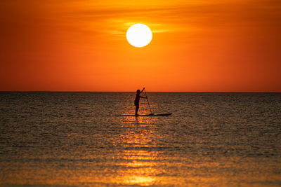 Silhouette person in sea against sky during sunset