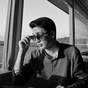 Portrait of young man looking through window at home