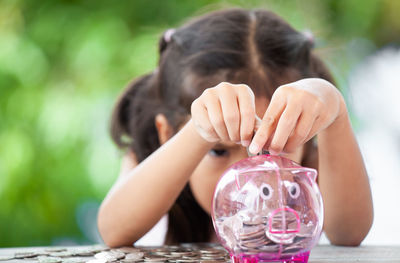 Girl putting coin in piggy bank at table