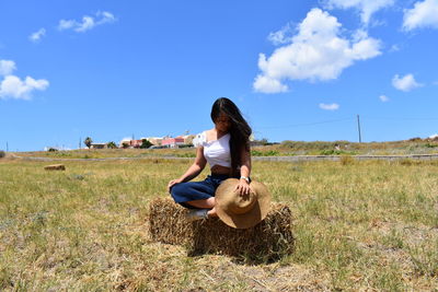 Young woman sitting on field against sky