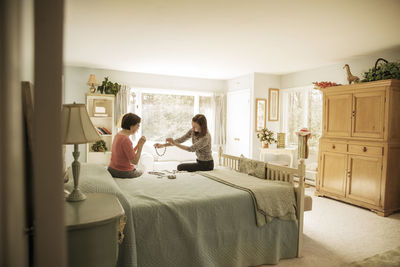 Mother and daughter looking at necklace while sitting on bed