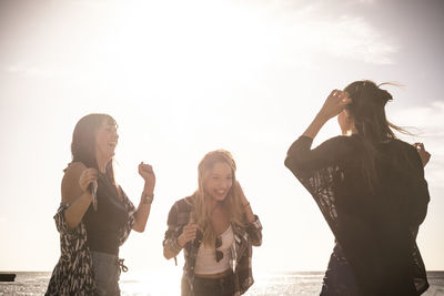 Young friends dancing at beach against sky