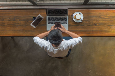 Rear view of man using mobile phone while sitting on table