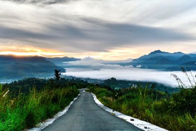 Road leading towards mountains against sky during sunset