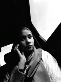 Portrait of young woman looking away while sitting on window