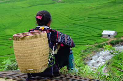 Rear view of woman with basket sitting against terraced field