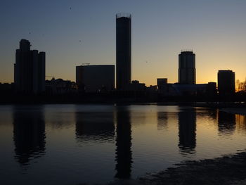 Silhouette buildings by lake against sky during sunset