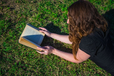 High angle view of woman reading book while lying on grass