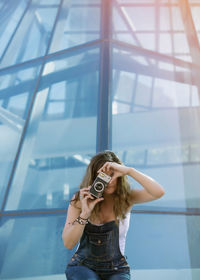 Woman holding camera while standing by window