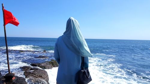 Rear view of man standing by sea against clear sky