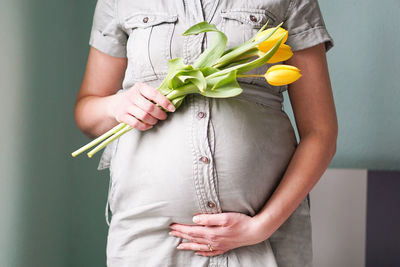 Pregnant woman with tulips flowers holding hands on belly on a pastel background. motherhood.