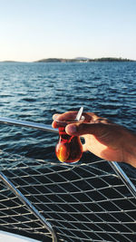 Cropped hand holding drink against sea