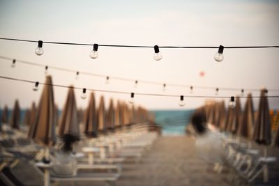 Street lights hanging from bridge against sky at dusk