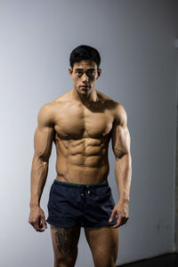 Portrait of shirtless muscular man standing against wall