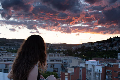 Woman standing by buildings against sky during sunset