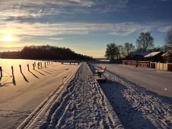 Snow covered road against sky during sunset