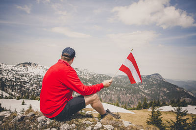 Rear view of man sitting on mountain against sky