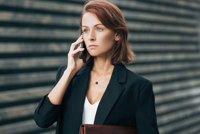 Young woman looking away while standing against wall