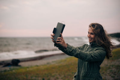 Smiling young woman taking selfie on digital tablet at beach