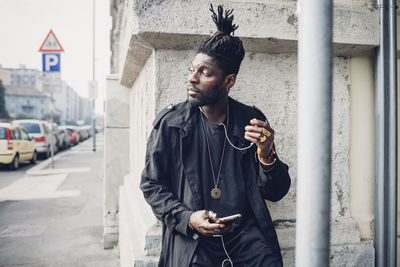 Fashionable man with mobile phone leaning on wall