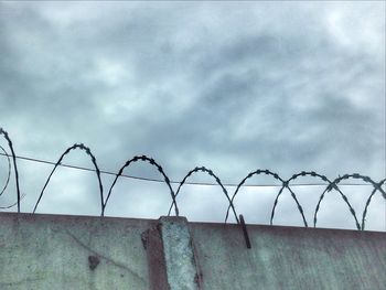 Barbed wire fence against cloudy sky