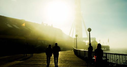 People on sidewalk in city against bright sun