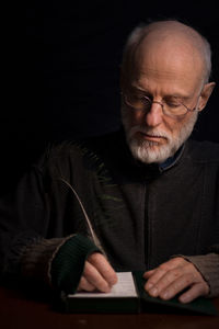 Mature man writing in paper at table against black background