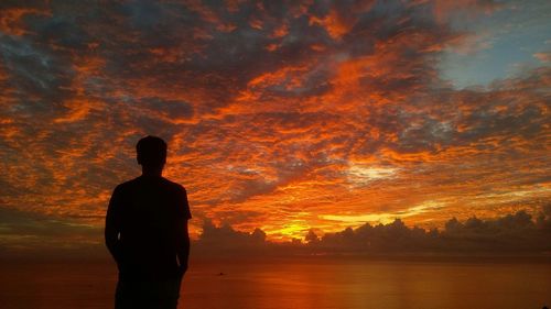 Silhouette man standing by sea against orange sky